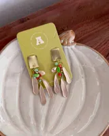 Caravanas colgantes con base cuadrada metálica dorada, decoradas con cuentas de colores y múltiples dijes colgantes alargados con textura.