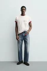 Camiseta blanca de corte relajado (relaxed fit) con cuello redondo y manga corta. Presenta un bolsillo plastrón en el pecho y un estampado de texto en color marrón rojizo en la espalda que dice "SOMETIMES SÍ, SOMETIMES BYE" (reemplazando la 'O' de 'SOMETIMES' por un corazón).