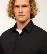 Camisa de manga corta con cuello inglés y cierre frontal abotonado, confeccionada en una mezcla de fibras de bambú, viscosa, poliéster y elastano. Presenta un diseño liso y entallado.