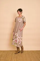 Vestido midi de lino color tostado con estampado floral en tonos rosados y verdes, cuello redondo, mangas cortas y bolsillos laterales.