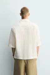 Camisa de corte relajado y boxy fit, confeccionada en tejido con textura irregular. Presenta cuello solapa, manga corta y cierre frontal con botones.