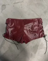 Short corto color bordó con efecto de cuero, tiro bajo, bolsillos frontales con cierre y detalle de hebilla con ojales metálicos.