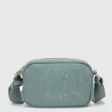 Cartera tipo bandolera de lona color rosado, con diseño rectangular y cierre superior. Presenta un logo circular grabado en el frente y correa ajustable con el nombre de la marca.