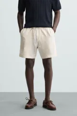 Bermuda de calce regular, color beige claro, confeccionada en tejido de mezcla de algodón con textura jacquard. Presenta cintura elástica ajustable con cordón, bolsillos frontales y un bolsillo trasero de vivo.