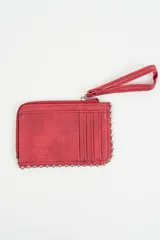 Billetera tipo tarjetero de cuero sintético color rojo, con cierre perimetral, correa de muñeca extraíble y detalle de tachas metálicas en el borde inferior y lateral. Presenta logo grabado en relieve.