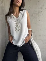 Blusa blanca sin mangas con cuello en V y detalle de puntilla en el ruedo. Cierre con botones.