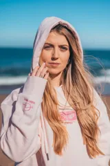 Hoodie rosa con capucha y cordones ajustables. Estampado en la espalda con un diseño de ondas, sol, concha marina y flores de hibisco.