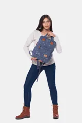 Mochila de lona azul con estampado floral, asas de mano superiores unidas por una tira con broche, detalles en cuero sintético marrón, bolsillo frontal con cierre y compartimentos laterales.