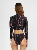 Crop top de bikini negro con estampado de cadenas rosas, cierre frontal con cremallera y detalle de flor en el cuello.