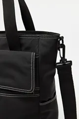Cartera tote negra con doble asa superior y correa desmontable y regulable. Cuenta con un bolsillo frontal con solapa y cierre, y bolsillos laterales. Presenta pespuntes blancos decorativos y un logo cuadrado en la parte inferior.