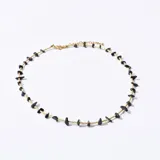 Gargantilla dorada con pequeñas cuentas y piedras negras irregulares.