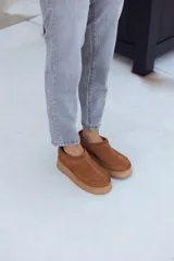 Calzado tipo sueco o zueco de cuero color óxido (marrón claro/camel), con diseño cerrado tipo mocasín y plataforma gruesa de goma color beige. Presenta un tirador de tela rojo en el talón.