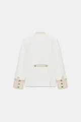 Chaqueta de estilo militar de ZARA Woman Collection, confeccionada en mezcla de algodón en color blanco y beige. Presenta cuello subido, manga larga con puños anchos en contraste y cierre frontal con alamares y botones metálicos en relieve. Tiene bajo asimétrico con abertura en la espalda.