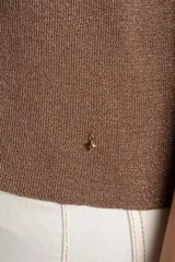 Sweater de tejido de punto fino en color arena, con cuello redondo y mangas cortas. Presenta un diseño minimalista con un pequeño detalle metálico en el ruedo.