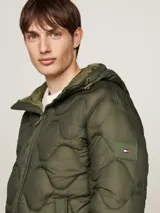 Campera acolchada verde militar con capucha fija y cordón ajustable, cierre de cremallera, dos bolsillos diagonales en la cintura y parche con el logo de Tommy Hilfiger en la manga. Repele el agua y cuenta con aislamiento térmico.