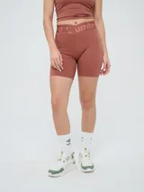 Biker deportiva Umbro para mujer, de color negro, confeccionada con tejido elástico y pretina cruzada con elástico personalizado de la marca.