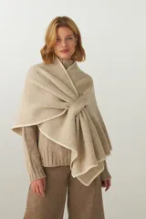 Ruana de tejido de punto industrial en color marrón, confeccionada en lana fina sin teñir. Presenta un diseño con doble ojal que permite mantener la prenda cruzada y cerrada.