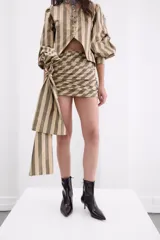 Minifalda de tafeta con diseño de rayas verticales en tonos bronce y beige. Presenta un estilo drapeado con un lazo lateral largo y caída fluida.