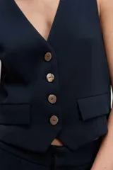 Chaleco sastrero de corte entallado, con diseño sin mangas y ajuste mediante hebilla metálica en la parte posterior.