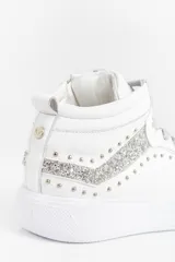 Zapatilla de caña media confeccionada en cuero vacuno blanco, con detalles de glitter plateado en los laterales y apliques de remaches metálicos. Cuenta con cierre lateral para facilitar el acceso y suela de caucho.