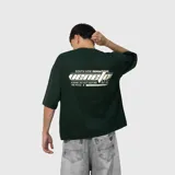 Remera de corte oversize color verde oscuro, con estampa gráfica en la espalda que incluye texto y diseño lineal.