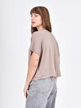 Remera de manga corta color beige claro, con cuello redondo y estampado floral en tonos dorados y plateados. Las mangas tienen un detalle de tejido acanalado.