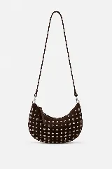 Bolso de hombro estilo hobo en color marrón oscuro, confeccionado en gamuza con diseño de tachas metálicas plateadas distribuidas por toda la superficie. Cuenta con un asa superior fija y cierre superior con cremallera.