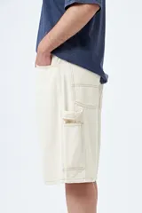 Bermuda de denim negro, estilo carpenter, con corte relajado y largo por encima de la rodilla. Presenta costuras visibles y múltiples bolsillos funcionales.