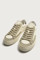 Zapatilla casual de tejido de algodón color beige con detalles en verde y un parche negro en el talón. Cuenta con suela de goma texturizada a contraste.