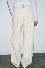 Jeans de tiro medio color blanco roto, con corte ancho y pierna recta. Presenta detalles de trabillas y pespuntes visibles, y bolsillos laterales y traseros.