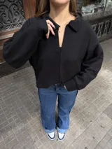 Buzo de punto color negro con cuello polo abierto, mangas largas y diseño holgado de corte corto.