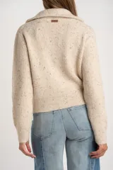 Cardigan de punto acanalado en color beige melange con motas oscuras. Presenta un diseño ajustado al cuerpo, cierre frontal completo con cremallera metálica y cuello alto.