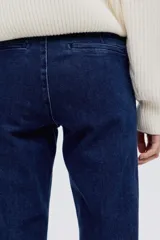 Jean de tiro alto con corte acampanado desde la rodilla. Presenta pliegues frontales y traseros, cierre con botón oculto y bolsillos traseros decorativos.