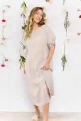 Vestido midi de lino color beige, con corte recto, cuello redondo y mangas 3/4 con botón. Presenta una hilera de botones decorativos en el frente y un tajo lateral.