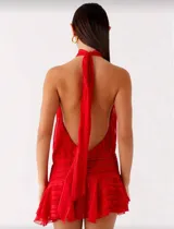 Vestido corto color rojo con cuello halter alto, espalda descubierta y falda con volados. Presenta un diseño con pliegues en la cintura y tejido fluido.