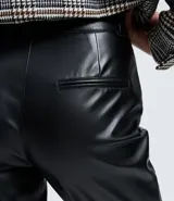 Pantalón de corte recto confeccionado en poliuretano con acabado que imita el cuero. Presenta cintura con trabillas, cierre frontal con botón y cremallera, bolsillos laterales y traseros, y detalle de abertura en el bajo.