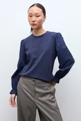 Remera de color blanco con cuello redondo y mangas largas abullonadas que presentan puños con volados.