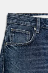Bermuda tipo jorts de denim con efecto lavado, tiro medio y corte holgado. Presenta diseño de cinco bolsillos, trabillas para cinturón, costuras laterales torcidas y cierre frontal con cremallera y botón metálico.