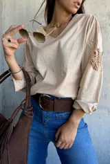 Blusa color beige con escote en V, manga larga y detalles de encaje calado en los hombros.