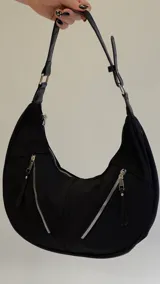 Cartera mediana negra de hombro con dos bolsillos externos con cierre y tiradores de cuero sintético. Cuenta con correa ajustable y herrajes metálicos plateados.