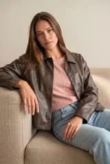 Campera de cuero vegano en tono marrón con acabado desgastado, corte recto y cierre frontal con botones a presión. Presenta cuello clásico y diseño minimalista.