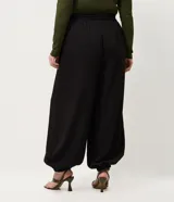 Pantalón de corte aladín confeccionado en crepé, de tiro alto con cintura elástica en la parte trasera. Presenta piernas anchas con volumen tipo globo que se estrechan en los tobillos mediante puños elásticos. Incluye bolsillos laterales funcionales.