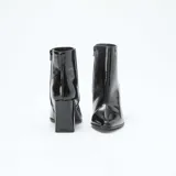 Botas de caña media en charol negro con acabado brillante, punta fina y taco cuadrado alto. Cuentan con cierre lateral interno.