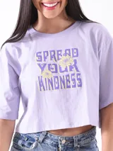 Remera crop top color lila con estampa frontal en tonos amarillos y violetas que incluye la frase 'Spread Your Kindness' y detalles florales.