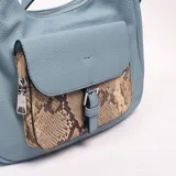 Bandolera de cuero sintético color celeste, de diseño hobo, con un bolsillo frontal con solapa de estampado animal print de serpiente y cierre con hebilla metálica. Incluye asa ajustable para llevar al hombro o cruzada.