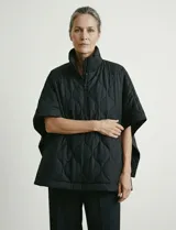 Poncho acolchado color vino tinto, con cuello alto y cierre frontal parcial. Presenta un patrón de costuras capitoné en forma de hoja o diamante y bolsillos delanteros.