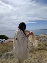 Ruana triangular tejida a crochet color crema con flecos largos.