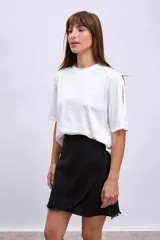 Minifalda color beige de corte evasé con diseño cruzado y detalle de flecos en el ruedo.