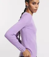 Suéter de punto color rosado, con cuello barco, mangas largas y puños con botones decorativos. El dobladillo también es acanalado.