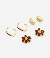 Set de tres pares de caravanas con baño en tono dorado. Incluye un par de aros en forma de corazón esmaltados en color bordó, un par de caravanas con diseño de flor esmaltada en bordó con centro texturizado y un par de caravanas tipo botón metálico liso.